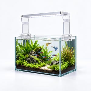 Puede incluir: Un acuario rectangular de cristal con estructura transparente y una lámpara LED plateada montada en la parte superior. El interior contiene sustrato oscuro, arena clara, rocas grises, plantas acuáticas verdes y varios peces pequeños de colores.