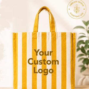 Pode incluir: Uma bolsa tote retangular de lona com listras verticais amarelas e brancas. O centro da bolsa exibe o texto Your Custom Logo em uma fonte marrom escura. A bolsa possui duas alças de tecido correspondentes na parte superior para transporte.
