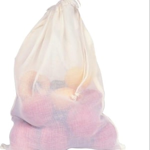 Puede incluir: Una bolsa con cordón de color crema, hecha de tela semitransparente, llena de fruta. La bolsa se cierra en la parte superior con un cordón blanco. Las frutas del interior parecen ser una mezcla de rojo y amarillo.