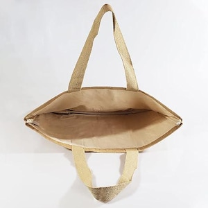 May include: A beige tote bag with two long handles and two shorter handles. The bag is made of a woven material and has a zippered closure. The interior of the bag is a lighter beige colour.