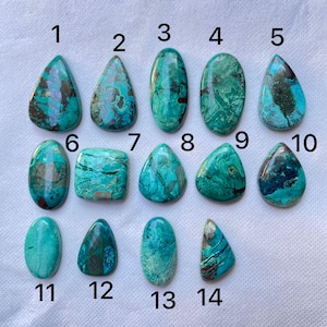 Puede incluir: Una colección de catorce piedras preciosas de crisocola pulidas en varias formas, incluyendo lágrimas, óvalos y un cuadrado. Las piedras muestran una mezcla de tonos turquesa, verde azulado y marrón, con patrones visibles. Cada piedra está numerada del 1 al 14.
