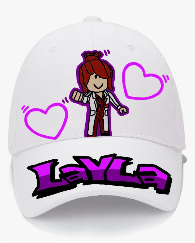 Puede incluir: Gorra de b&eacute;isbol blanca con un personaje de dibujos animados con pelo rojo y una bata de laboratorio, junto con dos contornos de coraz&oacute;n morados. El nombre "Layla" est&aacute; impreso en letras estilizadas moradas y negras.