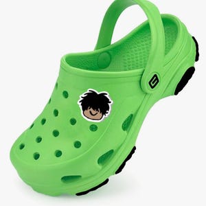 May include: Bright green clog-style shoe with a pivoting heel strap. The shoe features a cartoon sticker of a smiling face with black hair. The sole has black accents, and the shoe has ventilation holes.