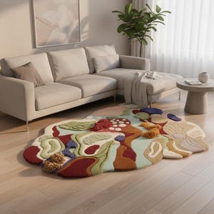 May include: An abstract, colorful rug with a unique, organic shape. The rug features a mix of textures and colors, including red, green, blue, and beige. It's placed on a light wood floor in a modern living room setting.