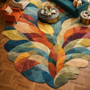 May include: A large, colorful area rug with a leaf design. The rug features shades of blue, green, orange, yellow, and red. The rug is placed on a hardwood floor and is surrounded by furniture, including a teal sofa and armchairs.