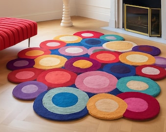 May include: A colorful, circular rug composed of various sized circles in shades of red, orange, yellow, blue, purple, and pink. The rug is placed on a light-colored wooden floor, creating a vibrant and playful aesthetic.