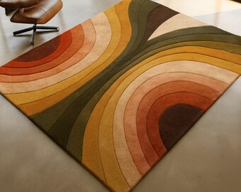 May include: A rectangular rug with a retro design. The rug features curved bands in shades of brown, orange, yellow, and green. The rug is placed on a neutral floor, and a brown leather chair is visible in the background.