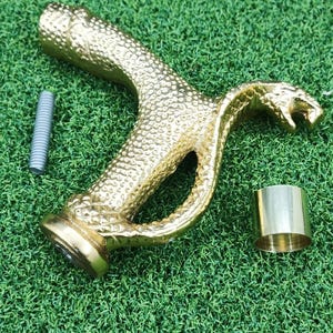 以下が含まれることがあります： 金色の蛇の形をしたハンドルで、表面はテクスチャ加工、銀色のネジ、金色の円筒形の部品があります。ハンドルは口が開いており、おそらく杖の装飾です。