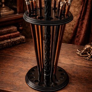 Pode incluir: Um suporte de madeira preto para bengalas, contendo v&aacute;rias bengalas com cabos decorativos. O suporte tem um design em camadas com um suporte central e uma base circular. As bengalas t&ecirc;m v&aacute;rios designs e cores de cabo.