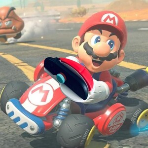 Peut inclure: Illustration numérique de Mario dans un kart rouge avec un logo "M" blanc, courant sur une route. Le kart a des pneus noirs et des accents bleus. Un personnage de Goomba est en arrière-plan. Mario porte une casquette et une salopette rouges.