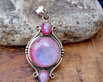 May include: A silver pendant with a large, round, pink and blue iridescent gemstone at the center. Two smaller pink gemstones are set above and below the central stone. The pendant has an ornate, curved silver frame.