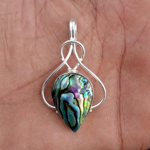 May include: A teardrop-shaped pendant featuring an iridescent abalone shell inlay set within a polished silver-toned metal frame. The metalwork consists of a smooth, curved bail and delicate wire loops that secure the colorful, swirling shell.