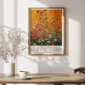 Puede incluir: Una impresión artística enmarcada con un diseño floral en tonos naranja, rojo, rosa y verde. La impresión incluye el texto "20th Century Exhibition" y "Gustav Klimt". La obra de arte se exhibe sobre una mesa de madera.