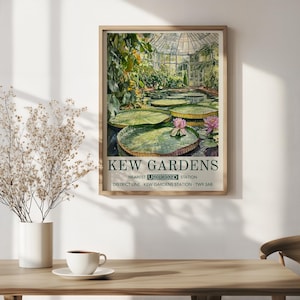 May include: A framed print of Kew Gardens, featuring a watercolour painting of a greenhouse with lily pads and pink flowers. The print includes the text "Kew Gardens" and "Nearest Underground Station". The frame is made of light-coloured wood.