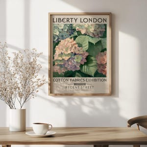 May include: A framed poster advertising "Liberty London" and a "Cotton Fabrics Exhibition". The poster features a watercolour painting of hydrangeas in pink, purple, and green. The poster is in a light brown wooden frame.