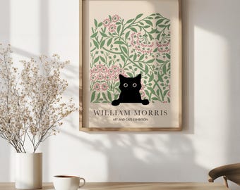 May include: A framed art print featuring a black cat peeking out from a floral design in green and pink. The print is labeled "WILLIAM MORRIS ART AND CATS EXHIBITION" in a serif font. The frame is a light wood color.