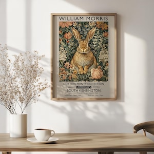 May include: A framed art print in the style of William Morris, depicting a brown rabbit amidst floral patterns. The print advertises a Cotton Prints Exhibition at South Kensington station.