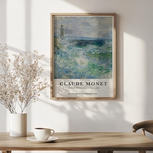 May include: Framed print of Claude Monet's "La Jette de Fécamp par gros temps." The artwork depicts a seascape with a lighthouse and crashing waves in shades of blue, green, and gray. The print is displayed in a wooden frame.