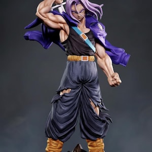 Puede incluir: Figura detallada de un personaje con pelo morado puntiagudo, que lleva una camiseta sin mangas negra, pantalones azules con rasgaduras y botas amarillas. El personaje sostiene una espada y una chaqueta morada está sobre los hombros. La figura posa sobre una base rocosa.