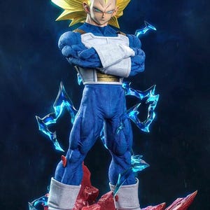 Puede incluir: Figura detallada de un personaje con pelo amarillo puntiagudo, armadura azul y blanca y pantalones azules. La figura posa con los brazos cruzados, de pie sobre una base rocosa roja con efectos de energía azul. El fondo es azul oscuro.