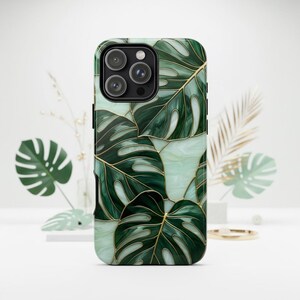 May include: A smartphone case featuring a pattern of dark green monstera leaves with gold-colored outlines set against a pale, marbled light green background. The case has a cutout for a triple-lens camera system on the upper left side.