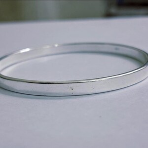Peut inclure: Un bracelet jonc argenté. Le bracelet a un design simple et circulaire avec une surface plate et polie. Le métal reflète la lumière, créant un aspect brillant. Ce bijou convient à un usage quotidien.
