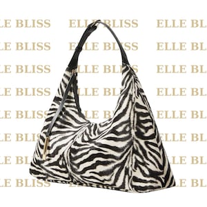 Puede incluir: Un bolso de hombro con estampado de cebra en blanco y negro con una correa negra y herrajes dorados. El bolso es de estilo suave y holgado con el texto "ELLE BLISS" repetido en el fondo.