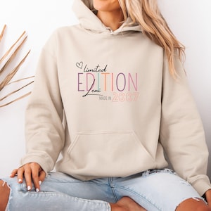 Könnte beinhalten: Beiger Kapuzenpullover mit Fronttasche und Kordelzug. Auf der Vorderseite steht in verschiedenen Farben und Schriftarten der Text "limited edition Jeni made in 2007", mit einem Herzsymbol über "limited".