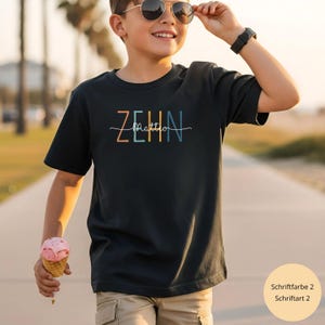 Könnte beinhalten: Schwarzes T-Shirt mit dem Wort "ZEHN" in Orange, Gelb und Blau und dem Namen "Mattio" in weißer Schrift. Die Person trägt eine Sonnenbrille und hält ein Eis in der Hand.
