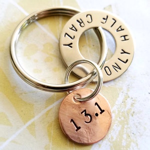 May include: A silver key ring with three charms. One charm is a silver ring with the words "HALF CRAZY ONLY" stamped on it. A copper-colored round charm has the numbers "13.1" stamped on it.