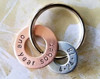 May include: A copper and silver keychain with two rings. The copper ring has the text "one year sober" engraved on it. The silver ring has the date "4.24.18" engraved on it.
