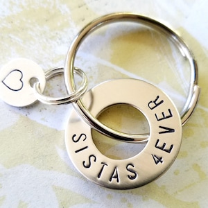 May include: Silver keychain with a heart charm and a washer charm with the words "Sistas 4 Ever" engraved on it.