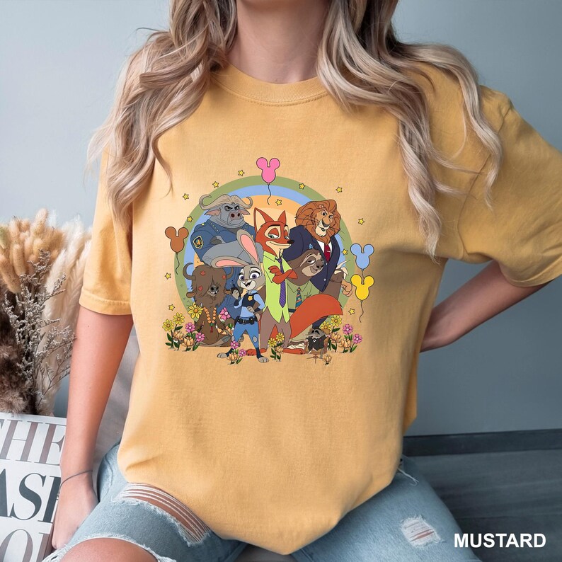Pode incluir: Camiseta mostarda com um gr&aacute;fico de desenho animado de personagens de um filme de anima&ccedil;&atilde;o popular. O design inclui v&aacute;rios personagens de animais, um arco-&iacute;ris e detalhes florais. A palavra "MUSTARD" &eacute; impressa no canto inferior direito.