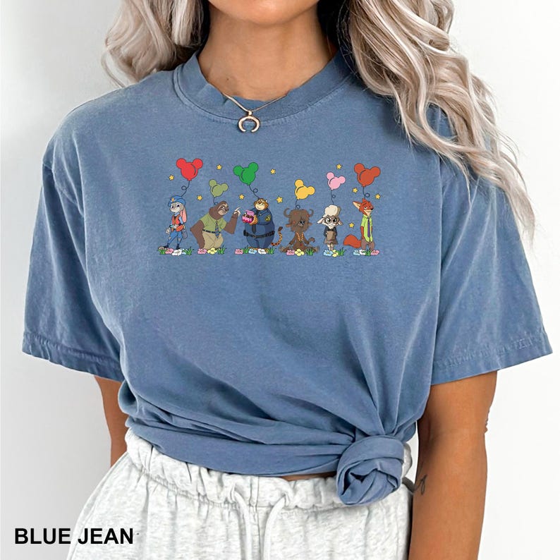 May include: A blue jean coloured t-shirt with a cartoon design of animals holding heart-shaped balloons. The shirt has a crew neck and short sleeves. The text "BLUE JEAN" is printed at the bottom of the image.