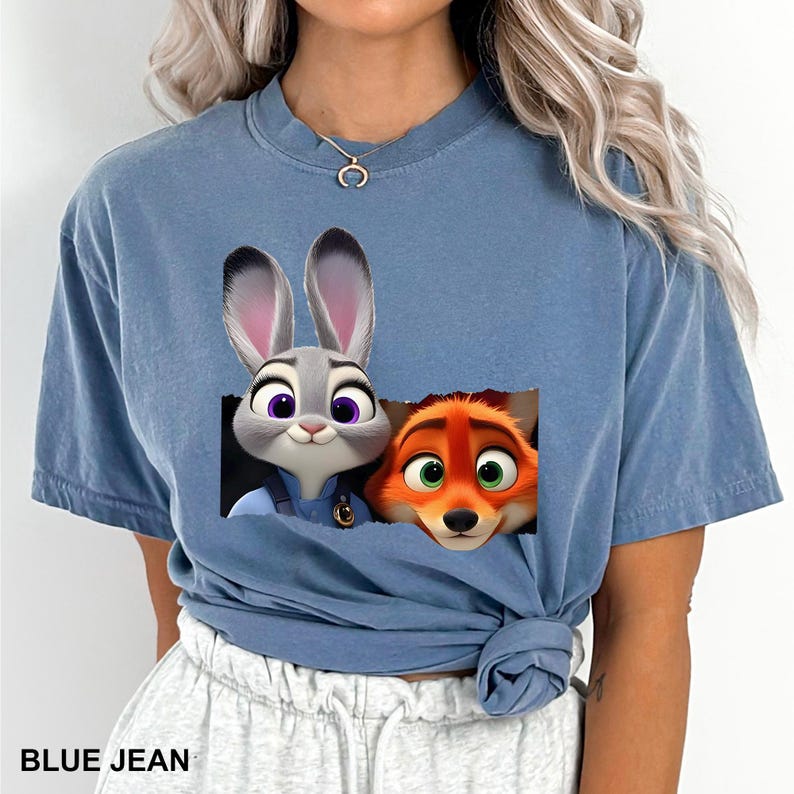 May include: Blue jean colored t-shirt featuring a graphic of Judy Hopps and Nick Wilde from Zootopia. The characters are in a rectangular design. The text "BLUE JEAN" is at the bottom of the shirt.