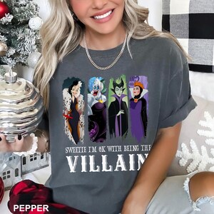 Puede incluir: Camiseta gris oscuro con cuatro personajes de villanos de dibujos animados. La camiseta tiene el texto blanco "Sweetie I'm OK with being the Villain". La camiseta es de estilo c&oacute;modo e informal.