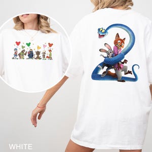 K&ouml;nnte beinhalten: Wei&szlig;es T-Shirt mit einem farbenfrohen Cartoon-Design auf der Vorderseite, das Figuren mit herzf&ouml;rmigen Luftballons zeigt. Auf der R&uuml;ckseite des Shirts ist eine blaue Schlange um einen Fuchs und ein Kaninchen gewickelt.
