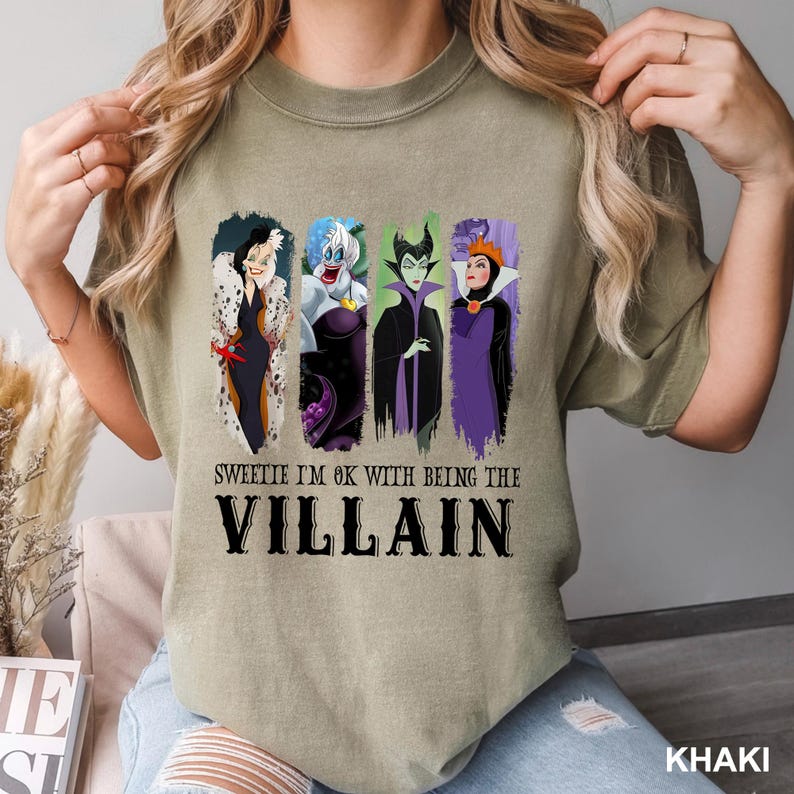 Puede incluir: Camiseta caqui con una ilustraci&oacute;n de cuatro villanos de dibujos animados y el texto "Sweetie I'm OK with being the Villain". La camiseta tiene cuello redondo y mangas cortas.