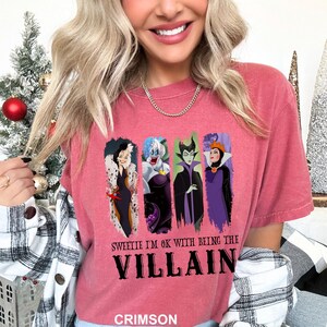 Puede incluir: Camiseta de color carmes&iacute; con cuatro personajes de villanos de dibujos animados. La camiseta tiene el texto "Sweetie I'm OK with being the Villain" en negro. La palabra "Crimson" est&aacute; impresa en la parte inferior de la camiseta.