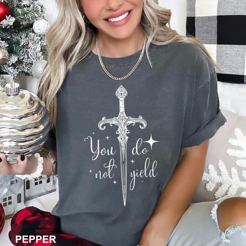Peut inclure: T-shirt gris fonc&eacute; avec une &eacute;p&eacute;e blanche et le texte "You do not yield". Le design pr&eacute;sente une illustration d&eacute;taill&eacute;e d'&eacute;p&eacute;e avec des &eacute;l&eacute;ments d&eacute;coratifs. Le t-shirt est de style d&eacute;contract&eacute;.