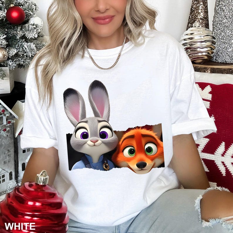 May include: White t-shirt featuring a graphic of Judy Hopps and Nick Wilde from Zootopia. Judy, a gray bunny, is on the left, and Nick, an orange fox, is on the right. The word "WHITE" is printed at the bottom of the shirt.