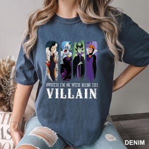 Puede incluir: Una camiseta azul denim con un gr&aacute;fico de cuatro villanos de dibujos animados. El texto "Sweetie I'm OK with being the Villain" est&aacute; impreso debajo de los personajes en letras blancas. La camiseta es de estilo casual.
