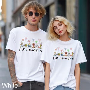 May include: White t-shirts with a "Friends" graphic featuring cartoon animals holding balloons. The text "F.R.I.E.N.D.S" is printed in black. The shirts are worn by two people.