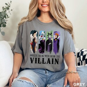 Puede incluir: Camiseta gris con un gr&aacute;fico de cuatro villanos de dibujos animados: Cruella de Vil, &Uacute;rsula, Mal&eacute;fica y la Reina Malvada. El texto "Sweetie I'm OK with being the Villain" est&aacute; impreso debajo.
