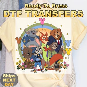 Pode incluir: Uma camiseta amarela com um design de transfer&ecirc;ncia DTF colorido com personagens de Zootopia. O design inclui Judy Hopps, Nick Wilde e outros personagens. O texto "Ready To Press DTF TRANSFERS" est&aacute; no topo.