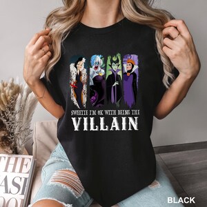 Puede incluir: Camiseta negra con un dise&ntilde;o de cuatro villanos de dibujos animados: Cruella de Vil, &Uacute;rsula, Mal&eacute;fica y la Reina Malvada. El texto dice: "Sweetie I'm OK with being the Villain".