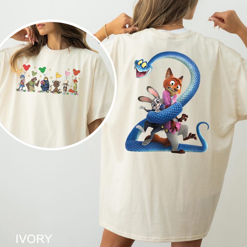 K&ouml;nnte beinhalten: Elfenbeinfarbenes T-Shirt mit farbenfroher Cartoon-Grafik. Auf der Vorderseite sind animierte Charaktere mit herzf&ouml;rmigen Luftballons abgebildet. Auf der R&uuml;ckseite ist eine blaue Schlange zu sehen, die sich um einen Fuchs und ein Kaninchen windet, mit der Zahl "2".