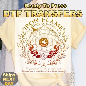 以下が含まれることがあります： Ready To Press DTF TRANSFERSという文字が入ったDTF転写デザインの薄い黄色のTシャツ。グラフィックは太陽の中央にドラゴンのアイコンがあり、雲、炎、月桂樹の枝に囲まれています。IRON FLAME BURN IT DOWNとThe first year is when some of us lose our lives. The second year is when the rest of us love our humanity.という文字が記されています。