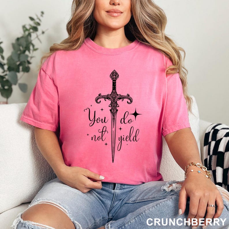 Peut inclure: T-shirt rose avec un motif d'&eacute;p&eacute;e noire et le texte &laquo; You do not yield &raquo;. Le t-shirt &agrave; manches courtes est fait d'une mati&egrave;re douce.