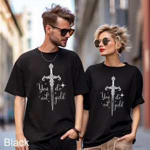 Peut inclure: T-shirts noirs avec un motif d'&eacute;p&eacute;e blanche et le texte "You do not yield". Les t-shirts sont &agrave; manches courtes et ont un col rond. Le motif comprend une illustration d&eacute;taill&eacute;e d'&eacute;p&eacute;e avec des &eacute;l&eacute;ments d&eacute;coratifs.